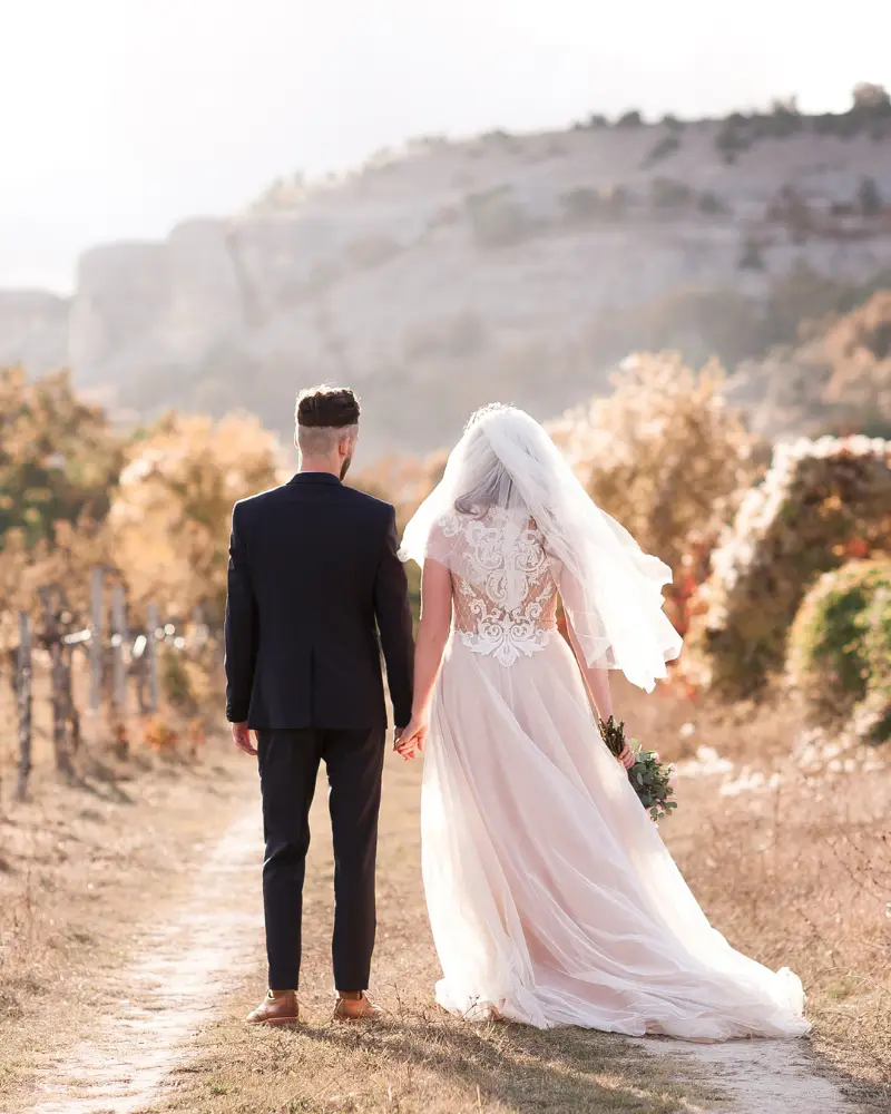 Zelf je bruiloft plannen, maar met een beetje hulp van mij (Femke) op de achtergrond. Ik ben geen typische weddingplanner, maar help jou terug naar rust en overzicht om weer heerlijk in jullie bruidsbubble te komen en relaxt je eigen bruiloft te organiseren. Foto: bruidspaar hand in hand op weg naar ceremonie.